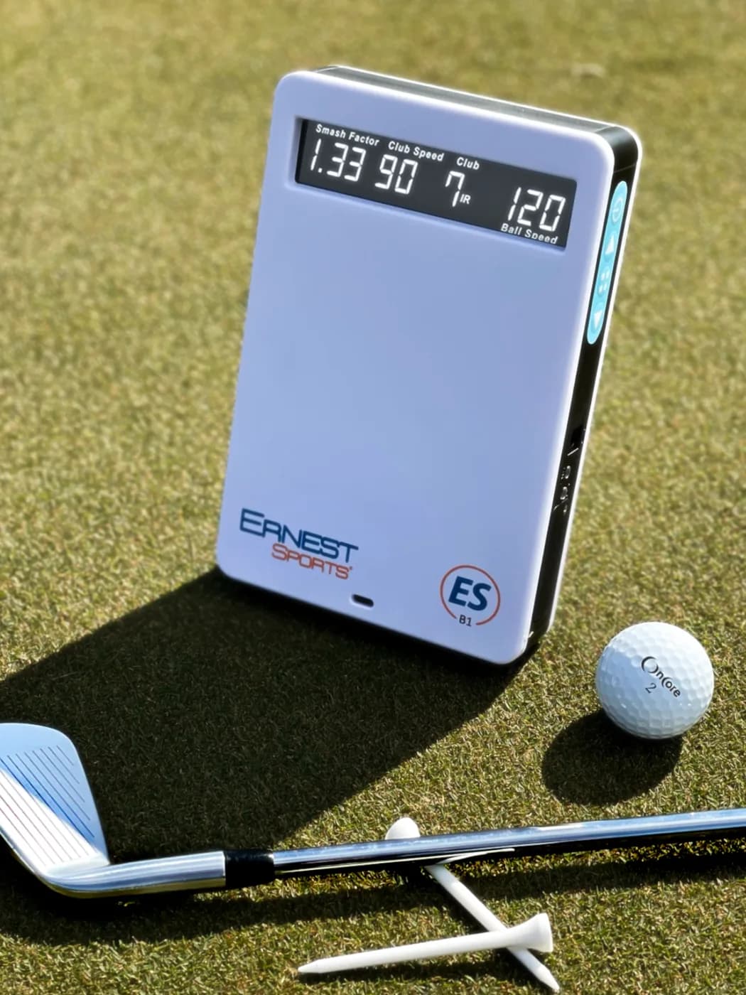 ESB1 launch monitor on the turf beside an iron and ball, its screen reading smash factor, club speed and ball speed