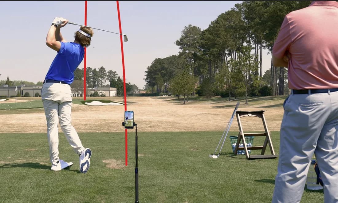Two golfers practising at a driving range with an Ernest Sports launch monitor on a stand